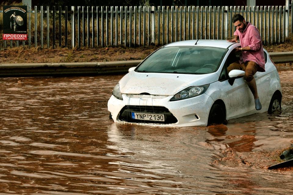 A man tries to get into a car stuck in floodwater in the town of Mandra. (Photo: Valerie Gache/AFP/Getty Images)