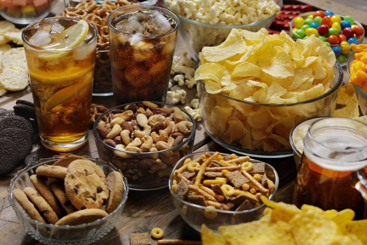 Selection of several different kinds of American junk food snacks with three different sodas including potato chips, M&Ms, chocolate chip cookies, popcorn, and oreos