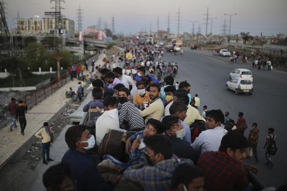 Trabajadores migrantes que se quedaron sin empleo por el coronavirus regresan a sus pueblos en el techo de un autobús mientras otros lo hacen caminando. Foto del 28 de marzo del 2020 tomada en las afueras de Nueva Delhi. (AP Photo/Altaf Qadri)