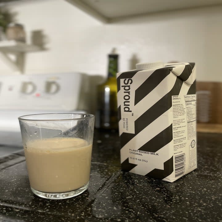 Glass of off-white Sproud next to carton