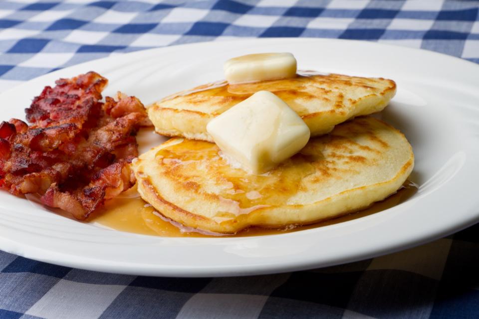 Pancakes with butter on top and grilled bacon served on a white plate.