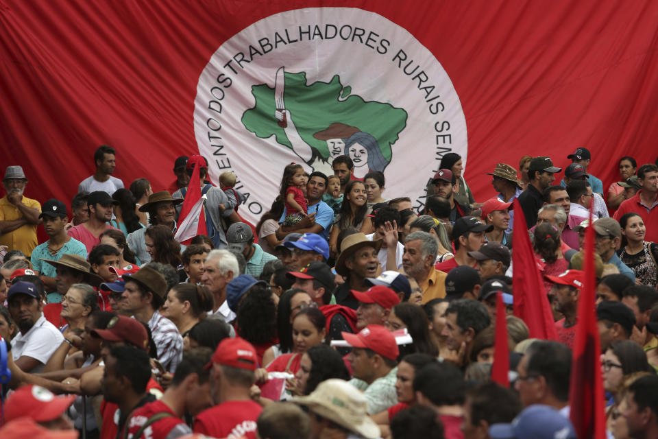 FILE - Supporters of Brazil's former President Luiz Inacio Lula da Silva backdropped by a Landless Workers' Movement banner, attend a rally in Quedas do Iguacu, Parana state, Brazil, March 27, 2018. Brazil's President Jair Bolsanaro accuses the movement, a key ally of da Silva, of illegally occupying others' landholdings. (AP Photo/Eraldo Peres, File)
