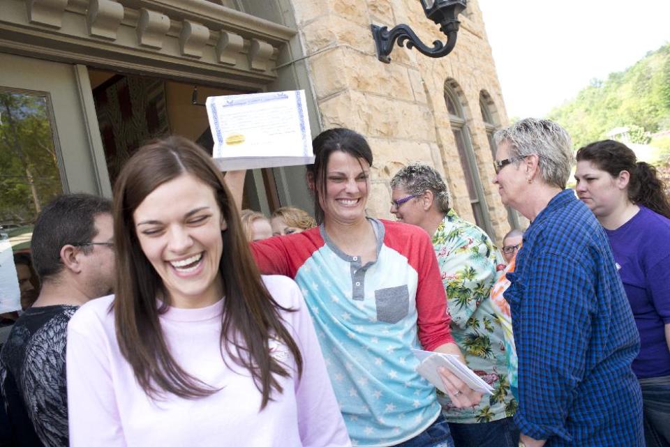 Kristin Seaton, center, of Jacksonville, Ark., holds up her marriage license as she leaves the Carroll County Courthouse in Eureka Springs, Ark., with her partner, Jennifer Rambo, left, of Fort Smith, Ark. Saturday, May 10, 2014, in Eureka Springs, Ark. Rambo and Seaton were the first same-sex couple to be granted a marriage license in Eureka Springs after a judge overturned Amendment 83, which banned same-sex marriage in the state of Arkansas. (AP Photo/Sarah Bentham)