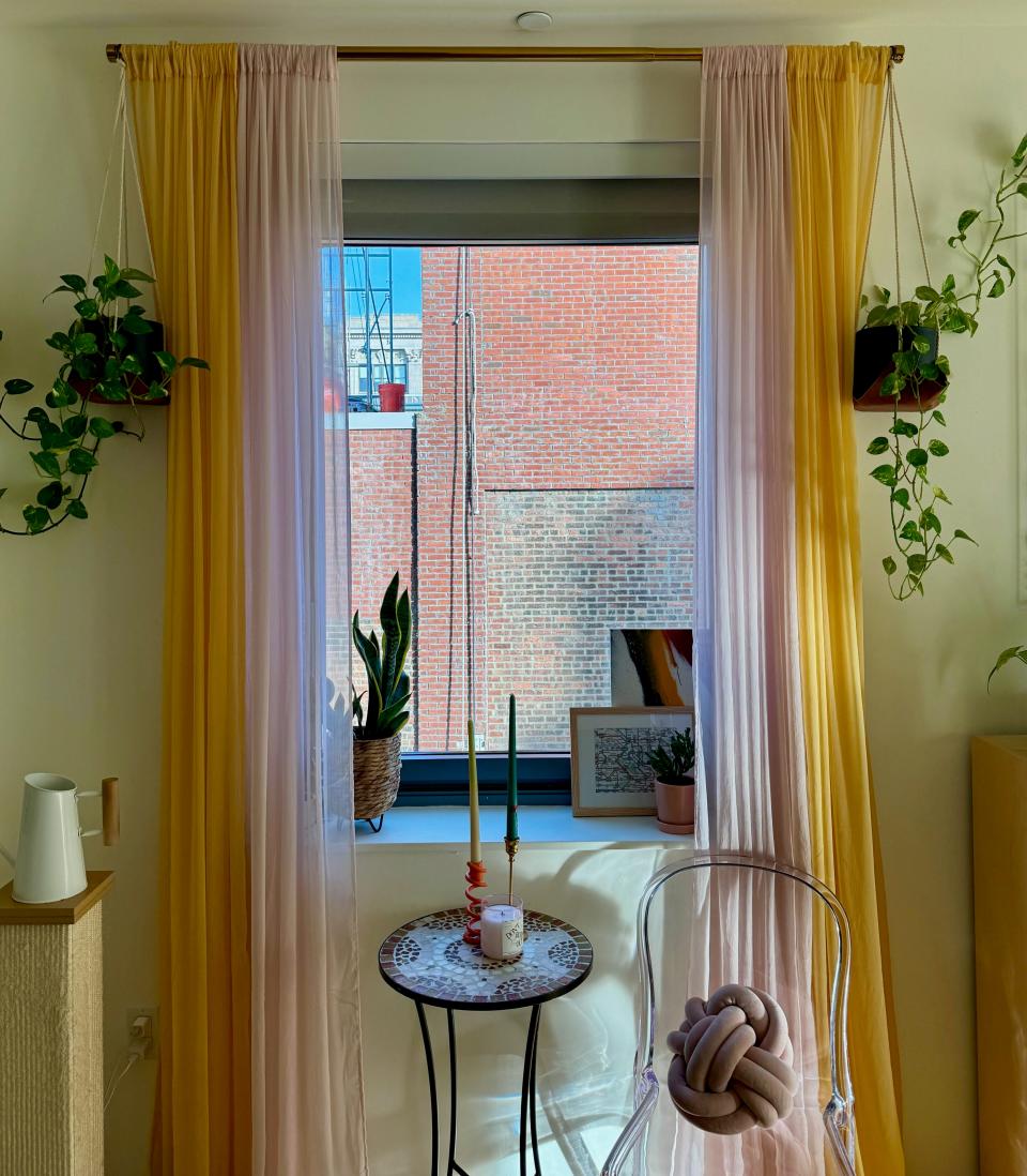 A nook by a window with pink and yellow curtains, a tale and a chair.