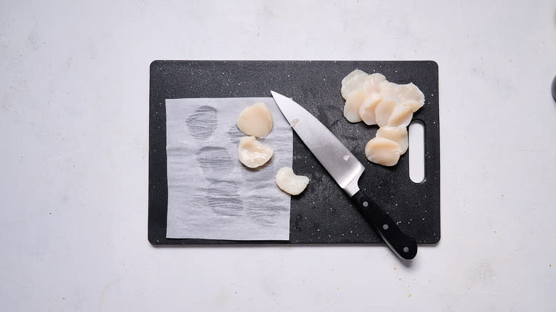 sliced raw scallops on cutting board with knife