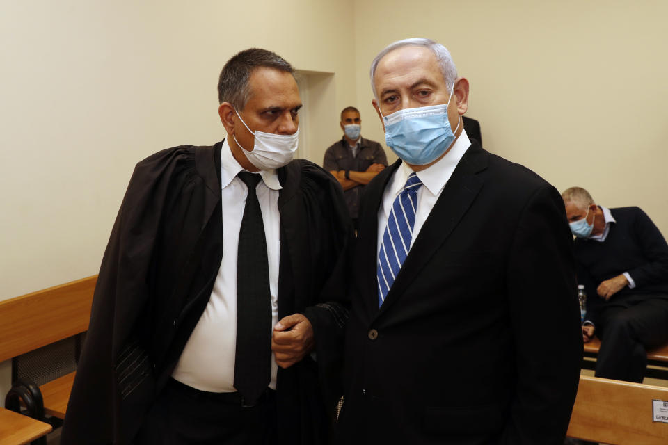 Israeli Prime Minister Benjamin Netanyahu, wearing a face mask in line with public health restrictions due to the coronavirus pandemic, stands inside the court room as his corruption trial opens at the Jerusalem District Court, Sunday, May 24, 2020. He is the country’s first sitting prime minister ever to go on trial, facing charges of fraud, breach of trust, and accepting bribes in a series of corruption cases stemming from ties to wealthy friends. (Ronen Zvulun/ Pool Photo via AP)