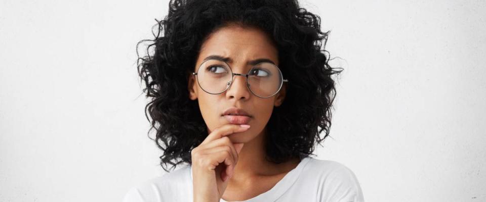 Isolated portrait of stylish young mixed race woman with dark shaggy hair touching her chin and looking sideways to make a decision
