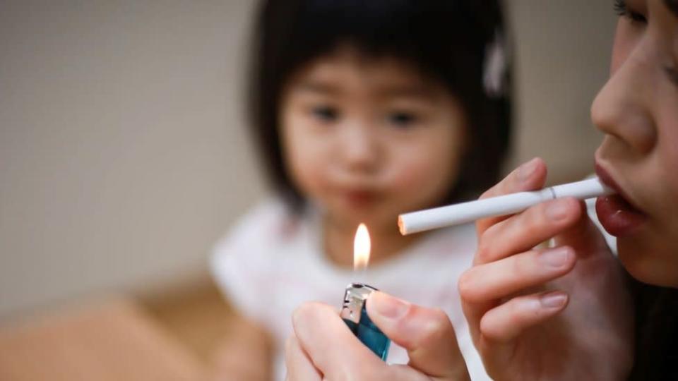 Mulher acende um cigarro em frente a uma criança muito pequena de olhos puxados