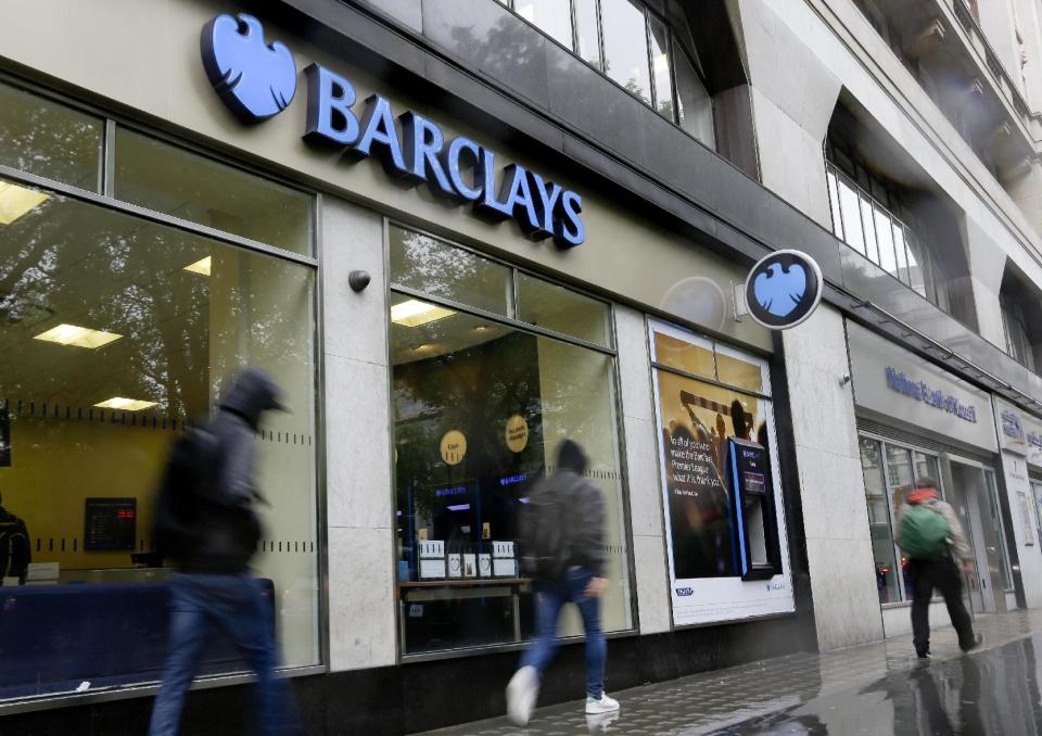 Pedestrians pass a branch of Barclays Bank in the rain in London, Thursday, May 8, 2014. British bank Barclays says it will cut around 14,000 jobs this year as it looks to streamline its operations and reduce the size of its investment banking arm. The figure was higher than anticipated — previously the bank had indicated that it was looking to get rid of between 10,000 and 12,000 people. (AP Photo/Kirsty Wigglesworth)