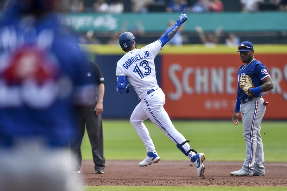 Lourdes Gurriel Jr. (13), de los Azulejos de Toronto, celebra su grand slam mientras recorre las bases y pasa frente al primera base de los Rangers de Texas, Andy Ibáñez, en la primera entrada del segundo juego de la doble cartelera en Buffalo, el domingo 18 de julio de 2021. (AP Foto/Adrian Kraus)