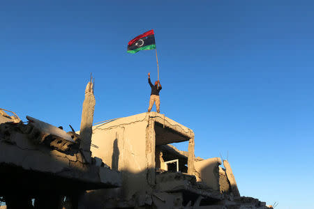 A fighter of Libyan forces allied with the U.N.-backed government waving a Libyan flag flashes victory sign as he stands atop the ruins of a house after forces finished clearing Ghiza Bahriya, the final district of the former Islamic State stronghold of Sirte, Libya. REUTERS/Hani Amara