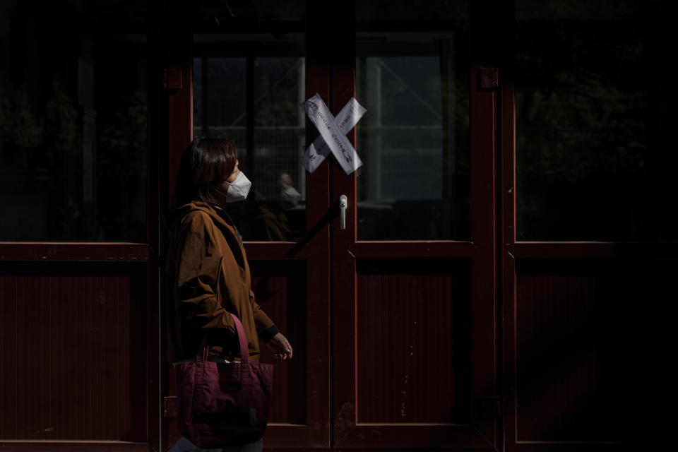 A woman wearing a face mask walks by a sealed shuttered shop lot in Beijing on Oct. 11, 2022. A meeting of the ruling Communist Party to install leaders gives President Xi Jinping, China's most influential figure in decades, a chance to stack the ranks with allies who share his vision of intensifying pervasive control over entrepreneurs and technology development. (AP Photo/Andy Wong)