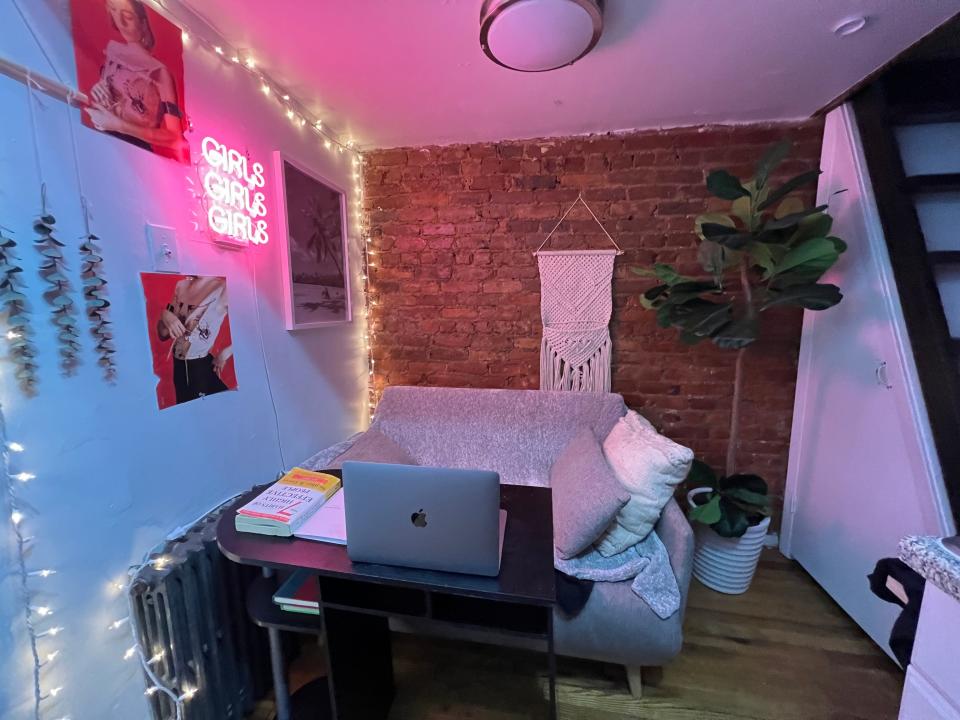 The living room of Alaina Randazzo's $650/month apartment, showing a small desk, small couch, and some wall decor