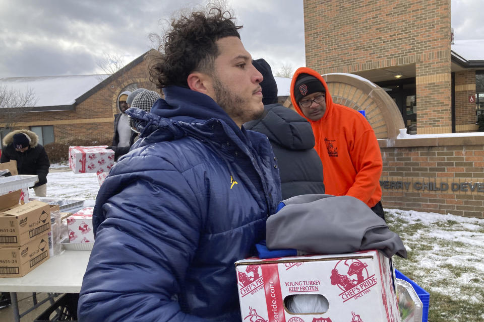 Michigan running back Blake Corum carries a tray containing a turkey, vegetables and other items during a giveaway event outside a school in Ypsilanti, Mich., on Sunday, Nov. 20, 2022. Corum took part in the charitable effort a day after hurting his knee and less than a week before his third-ranked Wolverines play No. 2 Ohio State. (AP Photo/Mike Householder)
