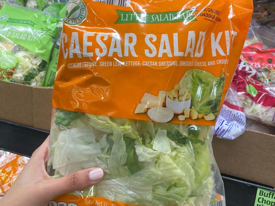 Hand holding orange and clear bag of caesar salad kit at Aldi