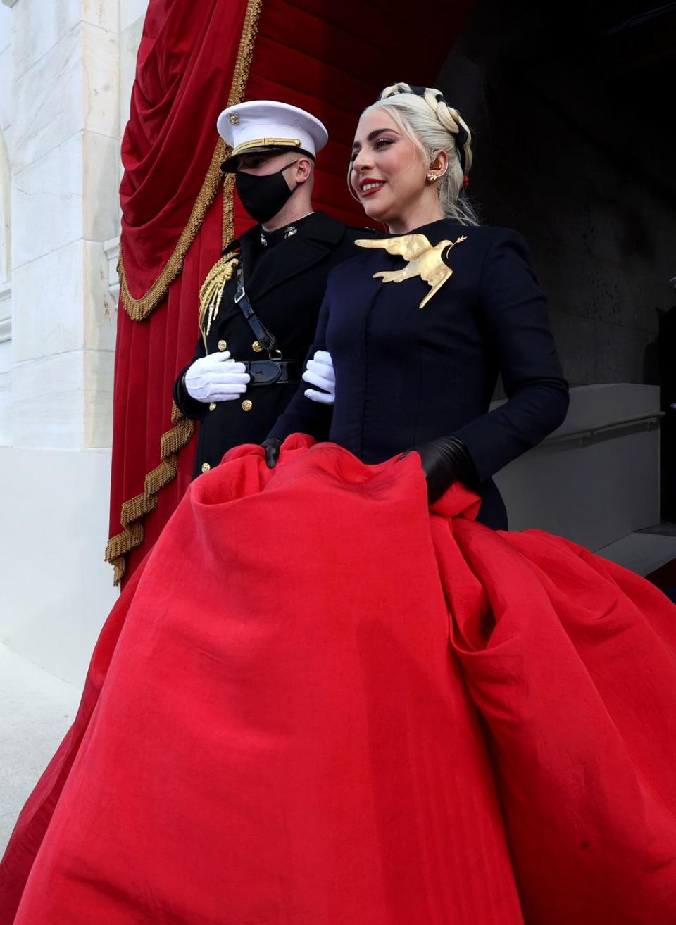 <p>The singer, who performed the National Anthem for the ceremony, made a dramatic addition to the day's order with a custom <a href="https://www.schiaparelli.com/en" rel="nofollow noopener" target="_blank" data-ylk="slk:Schiaparelli;elm:context_link;itc:0;sec:content-canvas" class="link ">Schiaparelli</a> couture look. The navy cashmere jacket and red silk voluminous skirt left an elegant mark, but the oversized dove and olive branch brooch, more importantly, nodded to the peace, gentleness, and purity that it symbolizes across many cultures. </p>