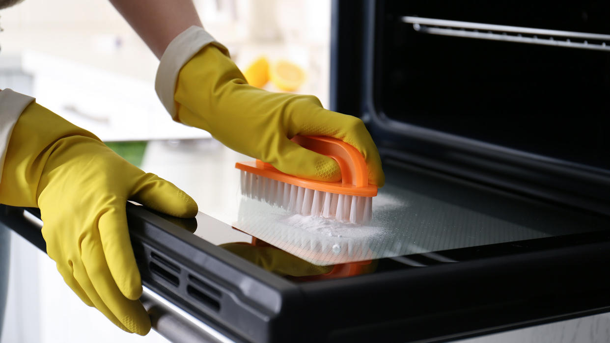  Person scrubbing the inside of an oven with a scourer brush and rubber gloves. 