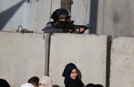 An Israeli border policeman keeps guard as a Palestinian girl waits with her mother to show their permits to Israeli security officers to make their way to attend the third Friday prayer of Ramadan in Jerusalem's al-Aqsa mosque, at Qalandia checkpoint near the West Bank city of Ramallah, July 3, 2015. REUTERS/Mohamad Torokman