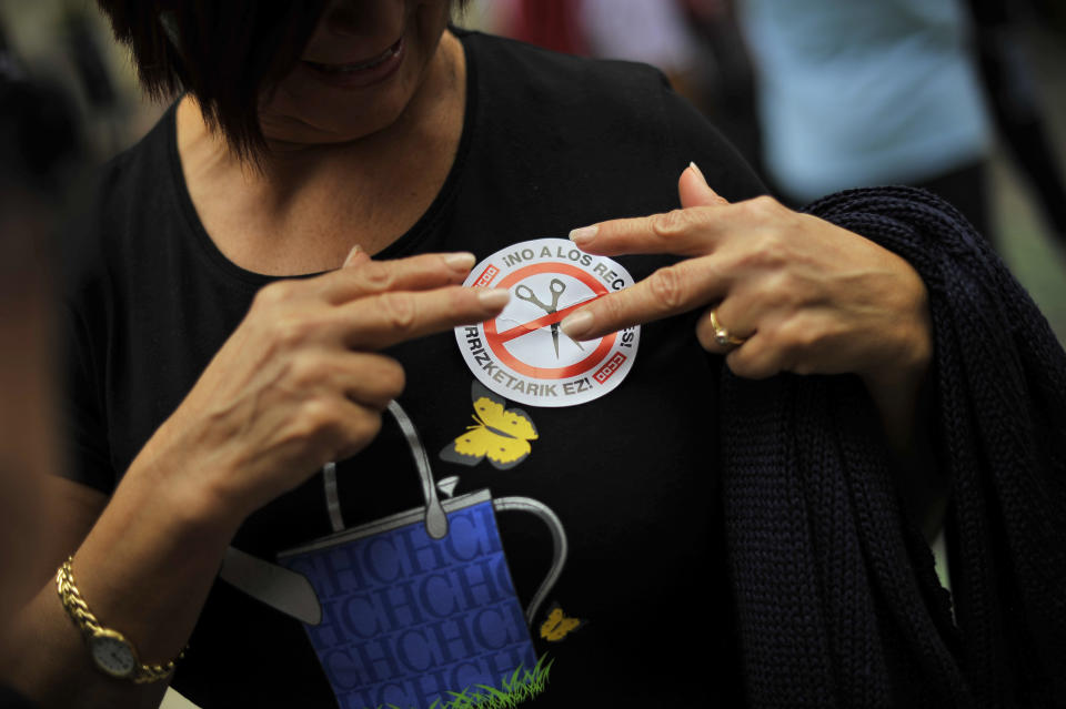 A citizen puts on her shirt a sticker against the Spanish Government's cutbacks plans, in Pamplona, northern Spain, Sunday, Oct. 7, 2012. Thousands of people called by 150 organizations are marching in 56 Spanish cities to protest punishing austerity cuts they say will only increase unemployment and job insecurity. (AP Photo/Alvaro Barrientos)