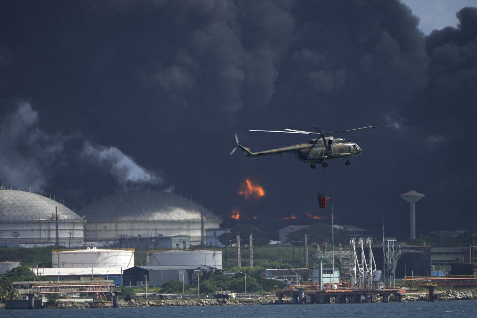 Un helicóptero arroja agua sobre la Base de Supertanqueros de Matanzas, mientras bomberos y especialistas trabajan para extinguir un incendio que fue causado por una tormenta eléctrica la víspera, en Matanzas, Cuba, el sábado, 6 de agosto del 2021. El incendio y cuatro explosiones asociadas dejaron más de 70 heridos. (AP Foto/Ramón Espinosa)