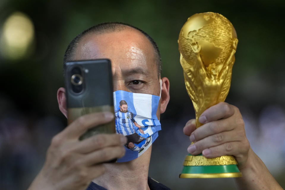 A man wearing a face mask with a picture of superstar Lionel Messi takes a selfie with a World Cup trophy replica as Chinese soccer fans wait to catch a glimpse of members of the Argentina national soccer team outside their hotel in Beijing, Tuesday, June 13, 2023. Argentina is scheduled to play Australia in a friendly match in China's capital on Thursday. (AP Photo/Andy Wong)