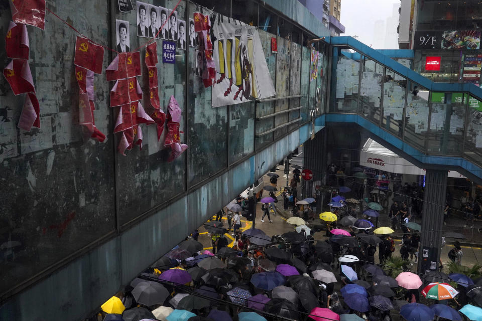 Protesters carrying umbrellas march past a pedestrian walk bridge displaying photos of tainted Chinese President Xi Jinping and communist party flags in Hong Kong, Sunday, Oct. 6, 2019. Thousands of protesters braved the rain to march in central Hong Kong as a second legal attempt to block a mask ban at rallies to quash four months of pro-democracy demonstrations was rejected by the court. (AP Photo/Vincent Yu)