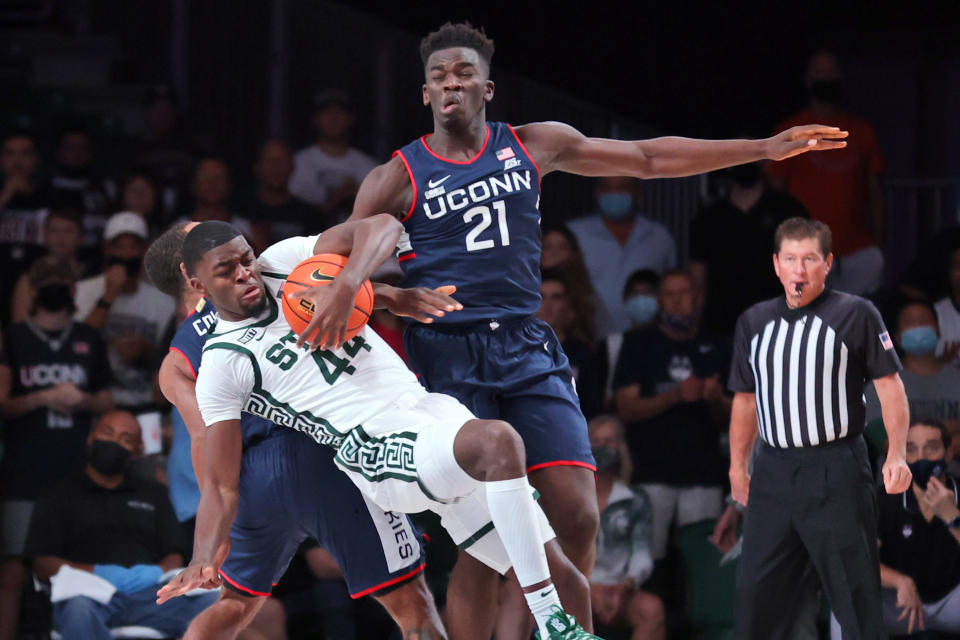 In this photo provided by Bahamas Visual Services, In a photo provided by Bahamas Visual Services, Michigan State forward Gabe Brown (44) falls to court after grabbing a rebound over Connecticut guard R.J. Cole, rear, and forward Adama Sanogo (21) during an NCAA college basketball game at Paradise Island, Bahamas, Thursday, Nov. 25, 2021. (Tim Aylen/Bahamas Visual Services via AP)