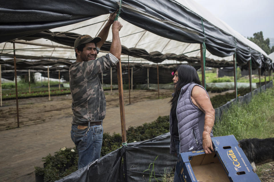 Elisa Xolalpa, quien sobrevivió a un ataque con ácido por su expareja hace 20 años cuando ella tenía 18 años, habla con un colega que también cultiva plantas en Ciudad de México, el sábado 12 de junio de 2021. (AP Foto/Ginnette Riquelme)