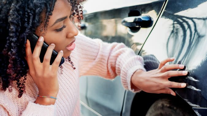 Black woman feeling sad after scratching car bodywork.