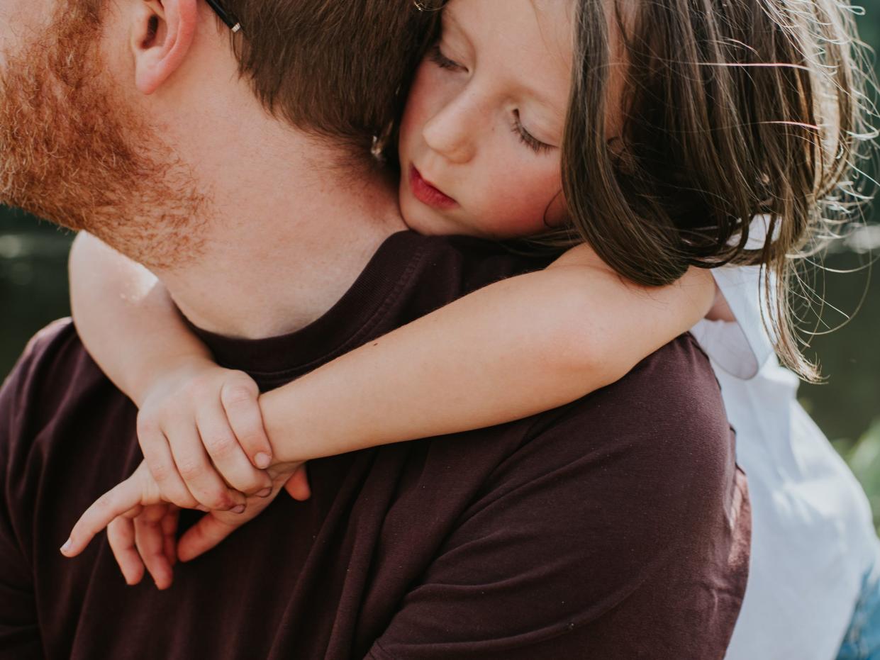 A daughter drapes her arms lovingly around her father's neck