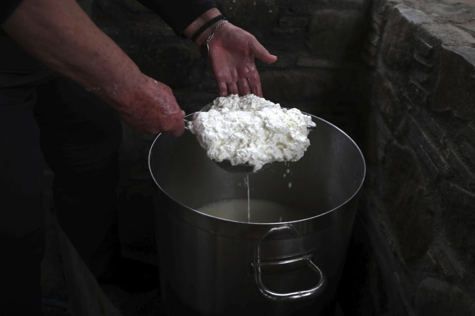 In this photo taken Wednesday Dec. 11, 2019, Aphrodite Philippou, 73, takes out cheese from a saucepan as she makes Cyprus' halloumi cheese at a farm in Kampia village near Nicosia, Cyprus. Cyprus' halloumi cheese, with a tradition dating back some five centuries, is the island nation's leading export. It's goat and sheep milk content makes it a hit with health-conscious cheese lovers in Europe and beyond. It's added appeal is that unlike other cheeses, it doesn't melt when heated up. (AP Photo/Petros Karadjias)