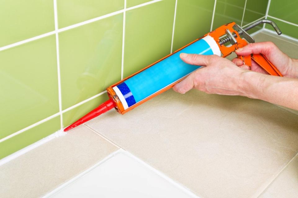 Person using caulk gun on tile in bathroom.