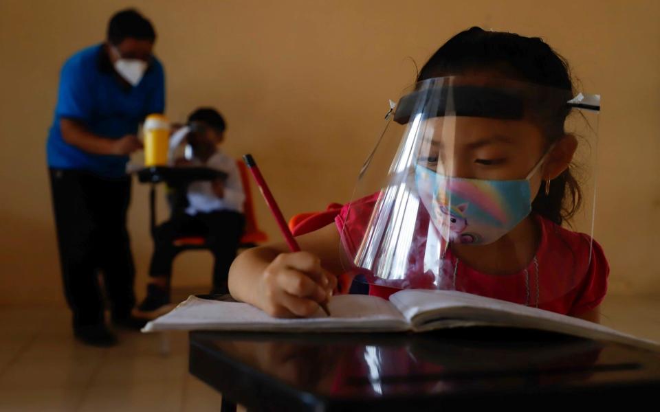 Wearing a mask and a face shield to curb the spread of the new coronavirus, 10-year-old Jade Chan Puc writes in her notebook during the first day of class in Montebello, Campeche state - the first region to transition back to the classroom after a year of remote learning due to the pandemic - AP Photo/Martin Zetina