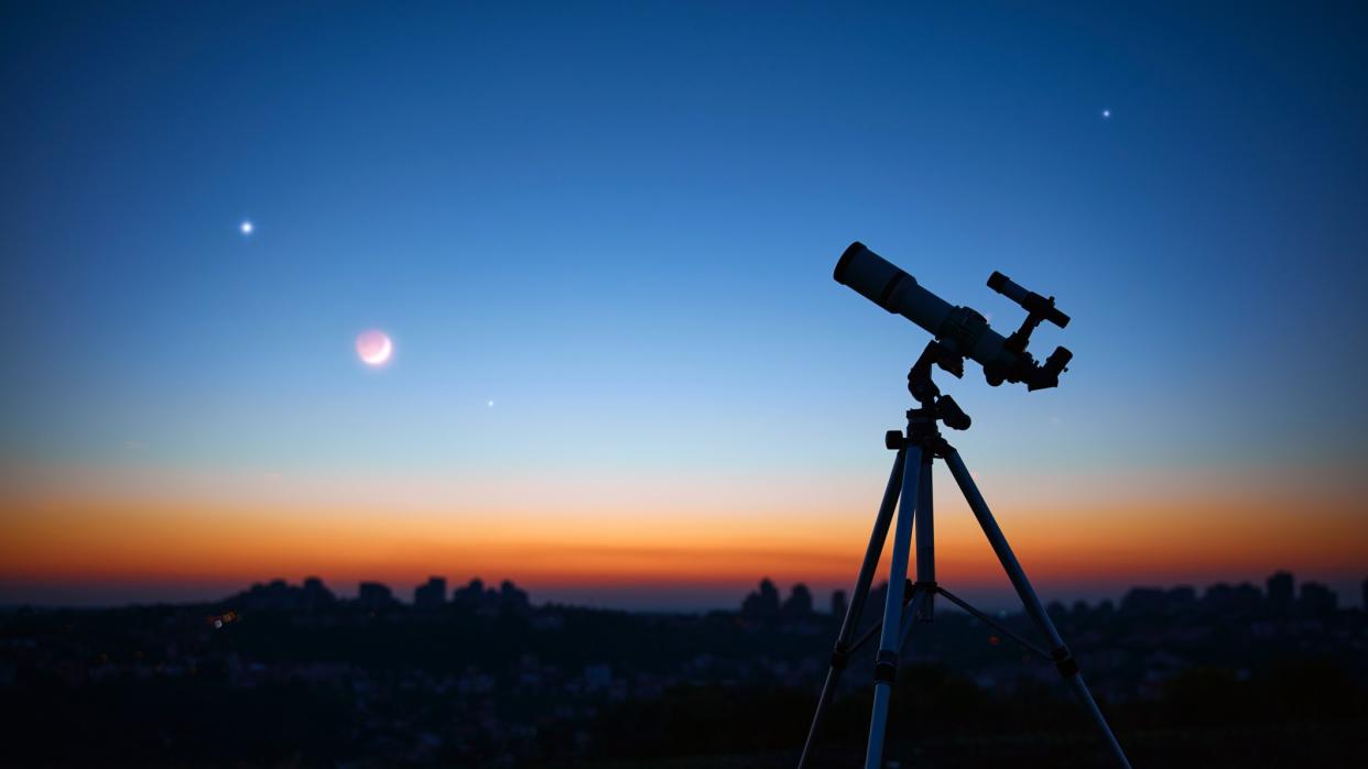  An image of a telescope standing in front of a sunset, with bright planets visible in the dimming sky 