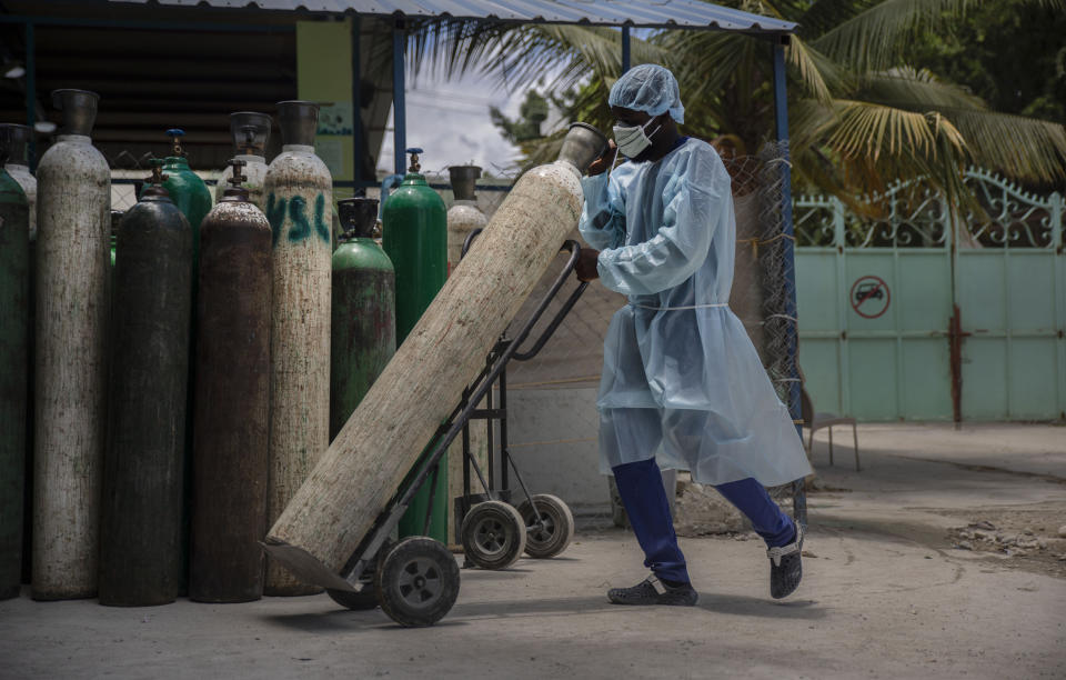 FILE - In this June 5, 2021, file photo, a hospital employee wearing protective gear transports oxygen tanks in Port-au-Prince, Haiti. In Haiti, hospitals are turning away patients as the country awaits its first shipment of vaccines. A major delivery via COVAX was delayed amid government concern over side effects and a lack of infrastructure to keep the doses properly refrigerated. (AP Photo/Joseph Odelyn, File)