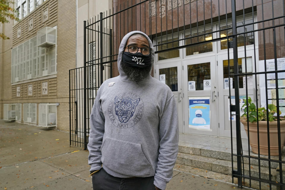 FILE - In this Monday, Oct. 26, 2020 photo, West Brooklyn Community High School principal Malik Lewis stands outside his school after students who showed up for the first day of reopening following a three-week coronavirus shutdown were dismissed in New York. The school was forced to close due to a spike in coronavirus cases in the immediate neighborhood. Although the school can handle up to 58 students under current restrictions, only 17 students showed up Monday. Lewis said many of his students care for younger siblings while their parents work or they have jobs so they're juggling a lot at once. He said he's disappointed but not surprised that few students have opted for in-person learning. (AP Photo/Kathy Willens, File)