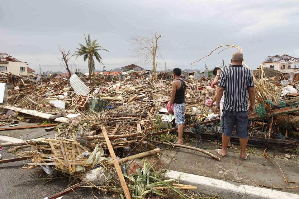 Survivors assess the damage after super Typhoon Haiyan battered Tacloban city, central Philippines November 9, 2013. Typhoon Haiyan, the strongest typhoon in the world this year and possibly the most powerful ever to hit land battered the central Philippines on Friday, forcing millions of people to flee to safer ground, cutting power lines and blowing apart houses. Haiyan, a category-5 super typhoon, bore down on the northern tip of Cebu Province, a popular tourist destination with the country's second-largest city, after lashing the islands of Leyte and Samar with 275 kph (170 mph) wind gusts and 5-6 meter (15-19 ft) waves. REUTERS/Romeo Ranoco (PHILIPPINES - Tags: DISASTER ENVIRONMENT)