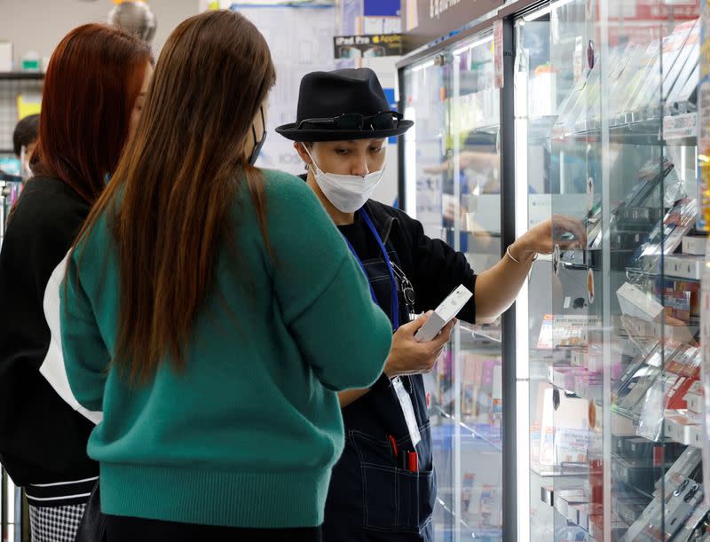 A clerk shows a used iPhone to customers from Thailand in Iosys Corp's shop selling used smartphones, in Tokyo