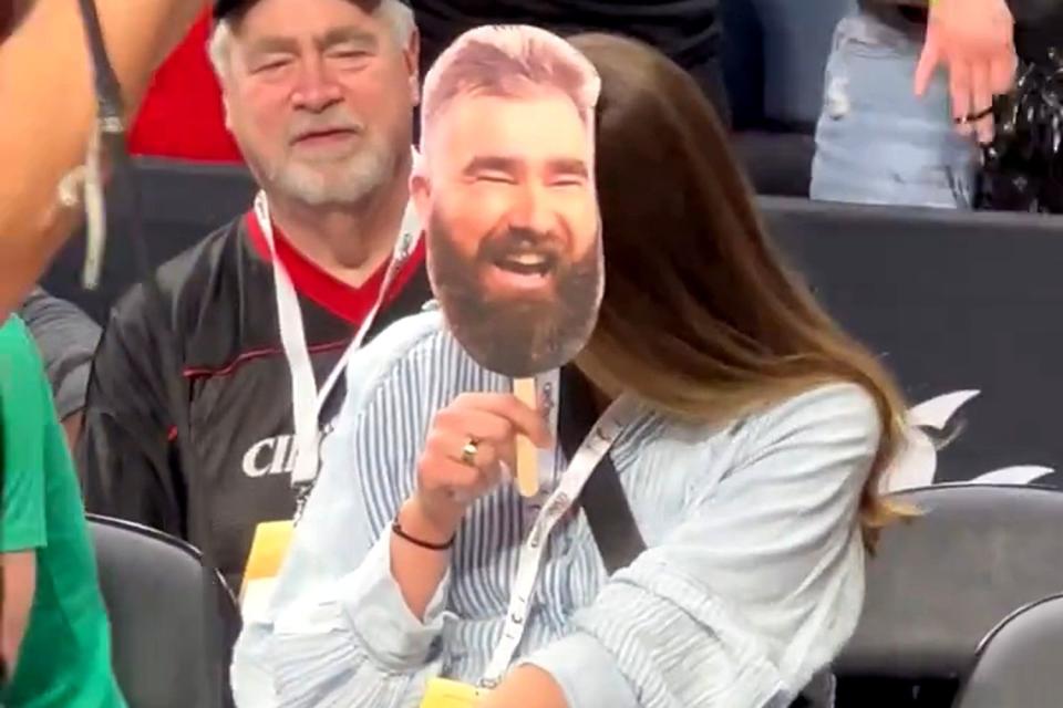 <p>New Heights/X</p> Kylie Kelce hiding behind a Jason Kelce mask