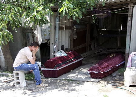 A man, whose mother according to locals was killed by an early morning shelling, reacts while sitting near her coffin, outside the damaged house before her funeral in Donetsk, Ukraine, in this July 7, 2015 file photo. REUTERS/Igor Tkachenko/Files