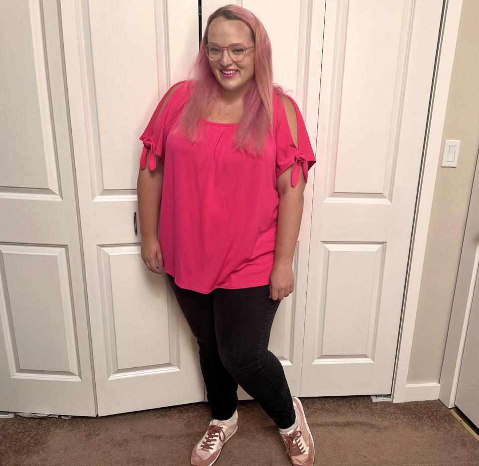 The writer wearing an oversized hot pink shirt, black leggings and light pink sneakers