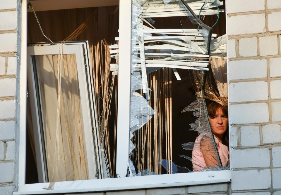 A woman looks through the shattered window of her flat (EPA)