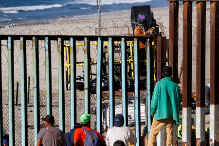 Migrants, part of a caravan of thousands trying to reach the U.S., look through the border fence between Mexico and the United States, as a welder reinforces the fence with concertina wire, in Tijuana, Mexico November 14, 2018. REUTERS/Jorge Duenes