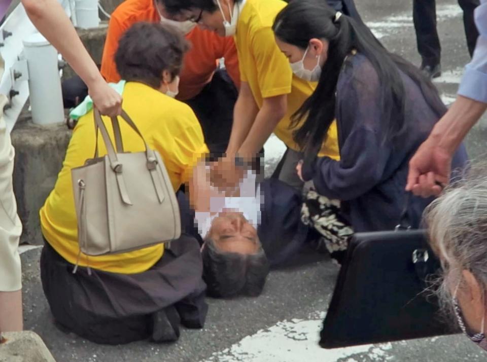 安倍晉三遭槍擊後躺在地上接受急救，身旁女子的深色罩衫內是黃色上衣、花紋長褲。圖片來源：共同社／路透