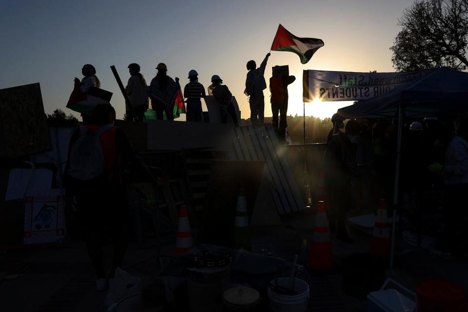 Protestors stand, two waving a Palestinian Flag, on the barricade set up on the eastern end of Dickson Court. Pro-Palestinian protesters clash with law enforcement as officials clear demonstrator encampments on UCLA's campus on May 2, 2024 in Los Angeles, Calif.