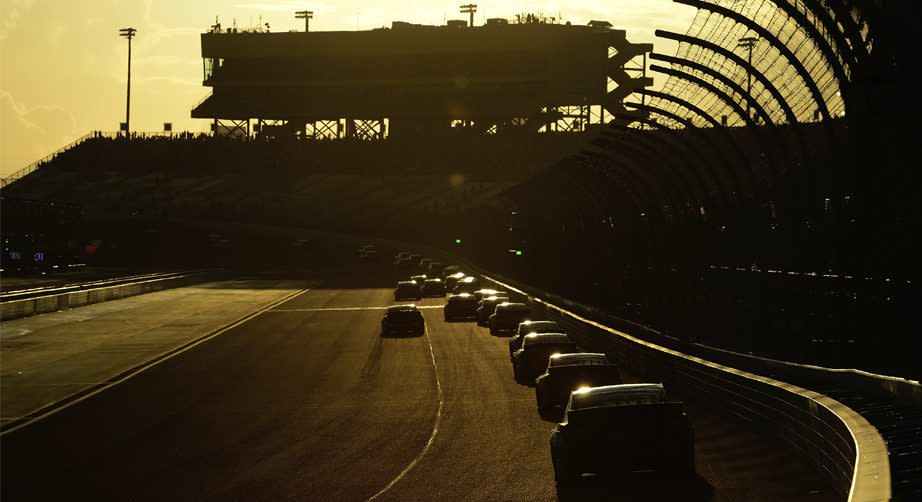 Cars race around the track as the sun sets.