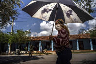 A woman wearing a mask amid the COVID-19 pandemic shades herself under the strong midday sun in Viñales, Cuba, March 1, 2021. Some Cubans are living on hope that new U.S. President Joe Biden will reverse at least some of the restrictions implemented by his predecessor. (AP Photo/Ramon Espinosa)