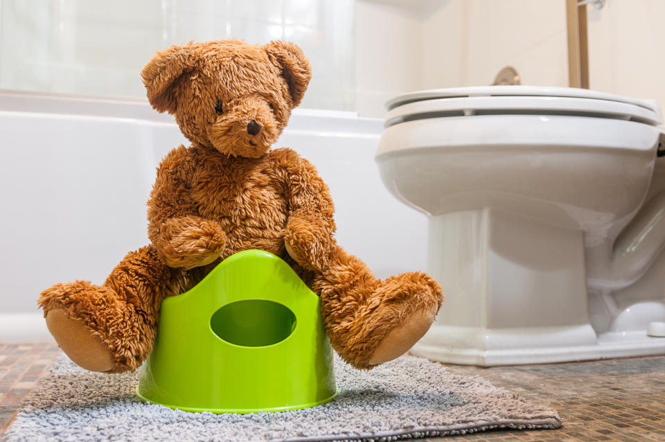 Teddy bear sitting on a small potty in a bathroom, representing potty training concept
