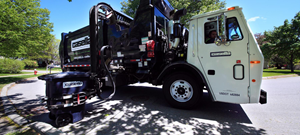 A Casella Waste Systems truck is shown collecting a refuse cart at the curb.