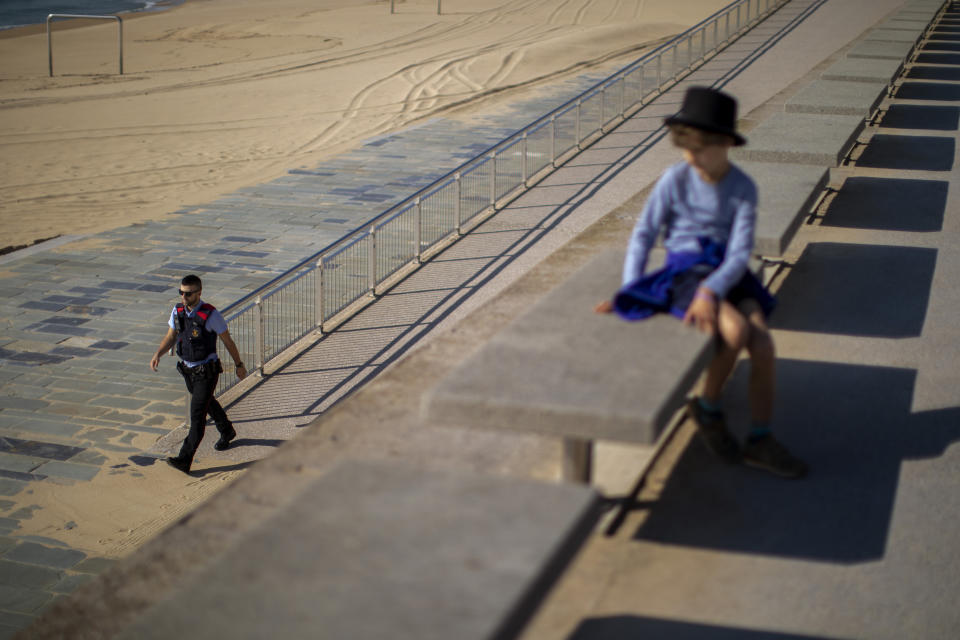 A child looks as a police officer patrols the promenade of the beach, where access is prohibited, in Barcelona, Spain, Sunday, April 26, 2020, as the lockdown to combat the spread of coronavirus continues. On Sunday, children under 14 years old will be allowed to take walks with a parent for up to one hour and within one kilometer from home, ending six weeks of compete seclusion. (AP Photo/Emilio Morenatti)